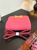 Hermes pink mini bag with gold H front clasp and red strap loop on tabletop.