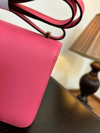 Hermes pink mini bag close-up of textured leather with red strap and metal buckle.
