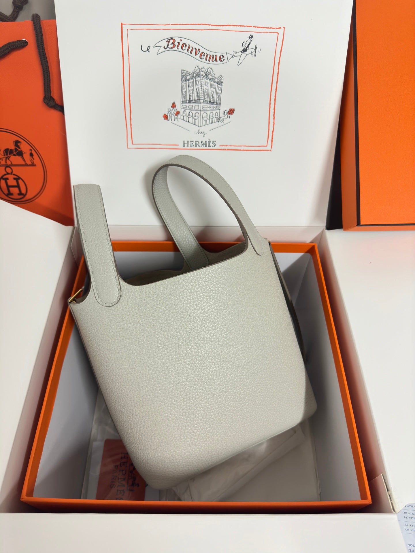 Hermes pale gray leather tote bag in box, front view with handle cutouts