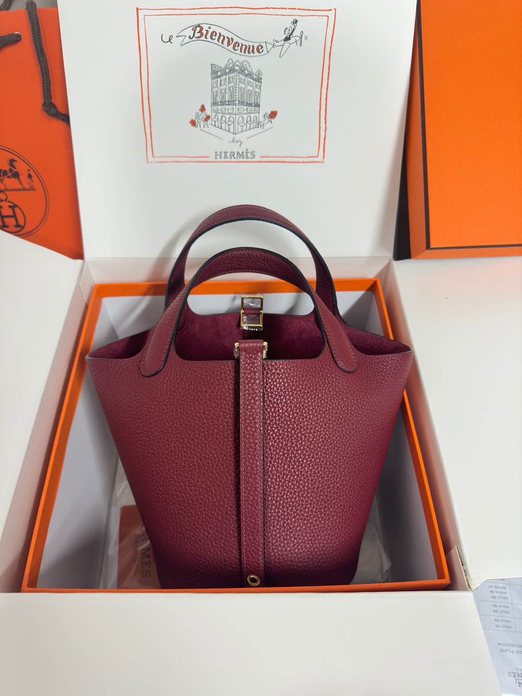 Burgundy textured leather tote bag with front strap detail and top handles