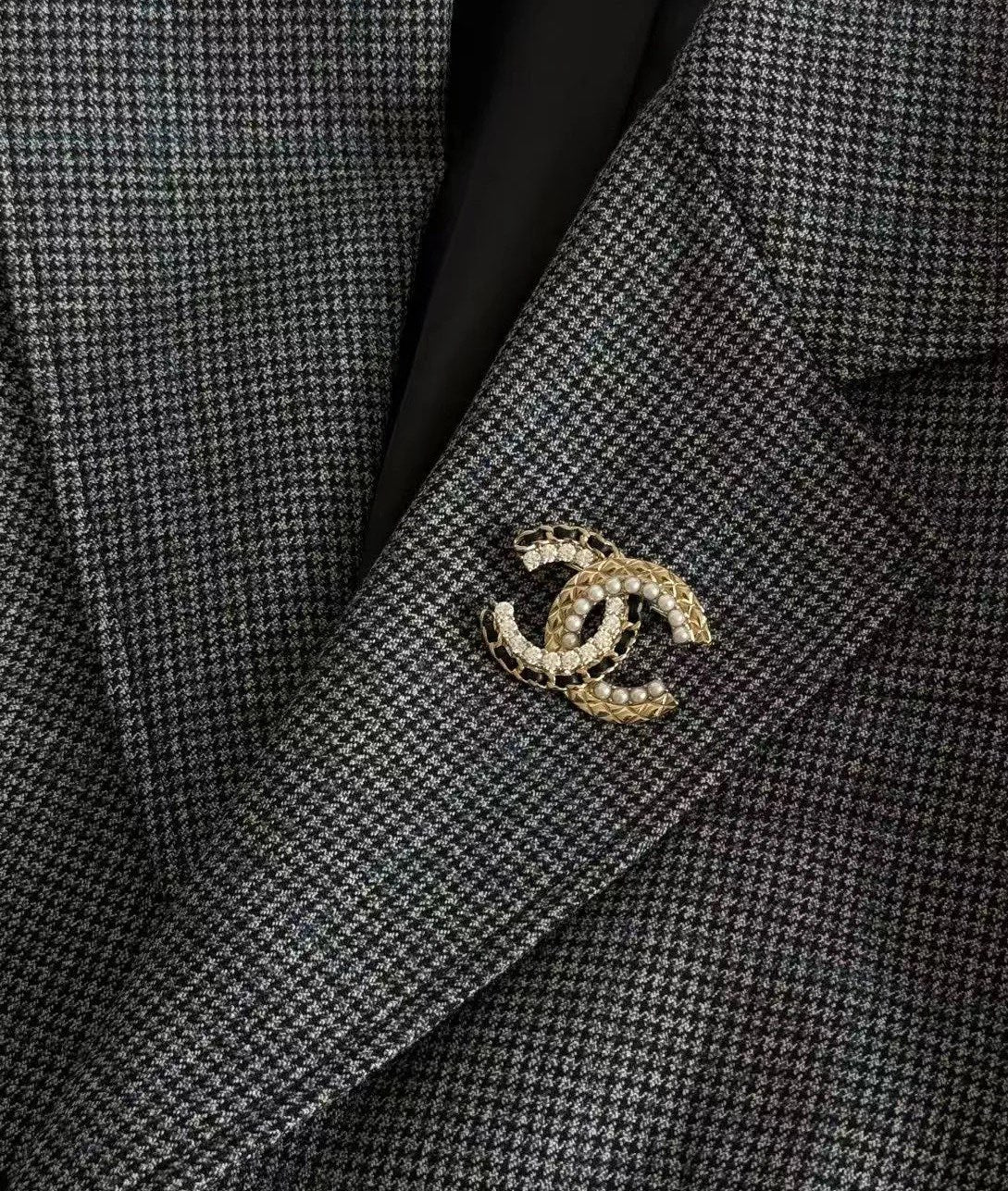 Gold-tone interlocking C brooch with crystal and pearl details on grey blazer lapel