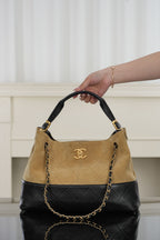 Tan and black quilted shoulder bag held by top handles with chain links