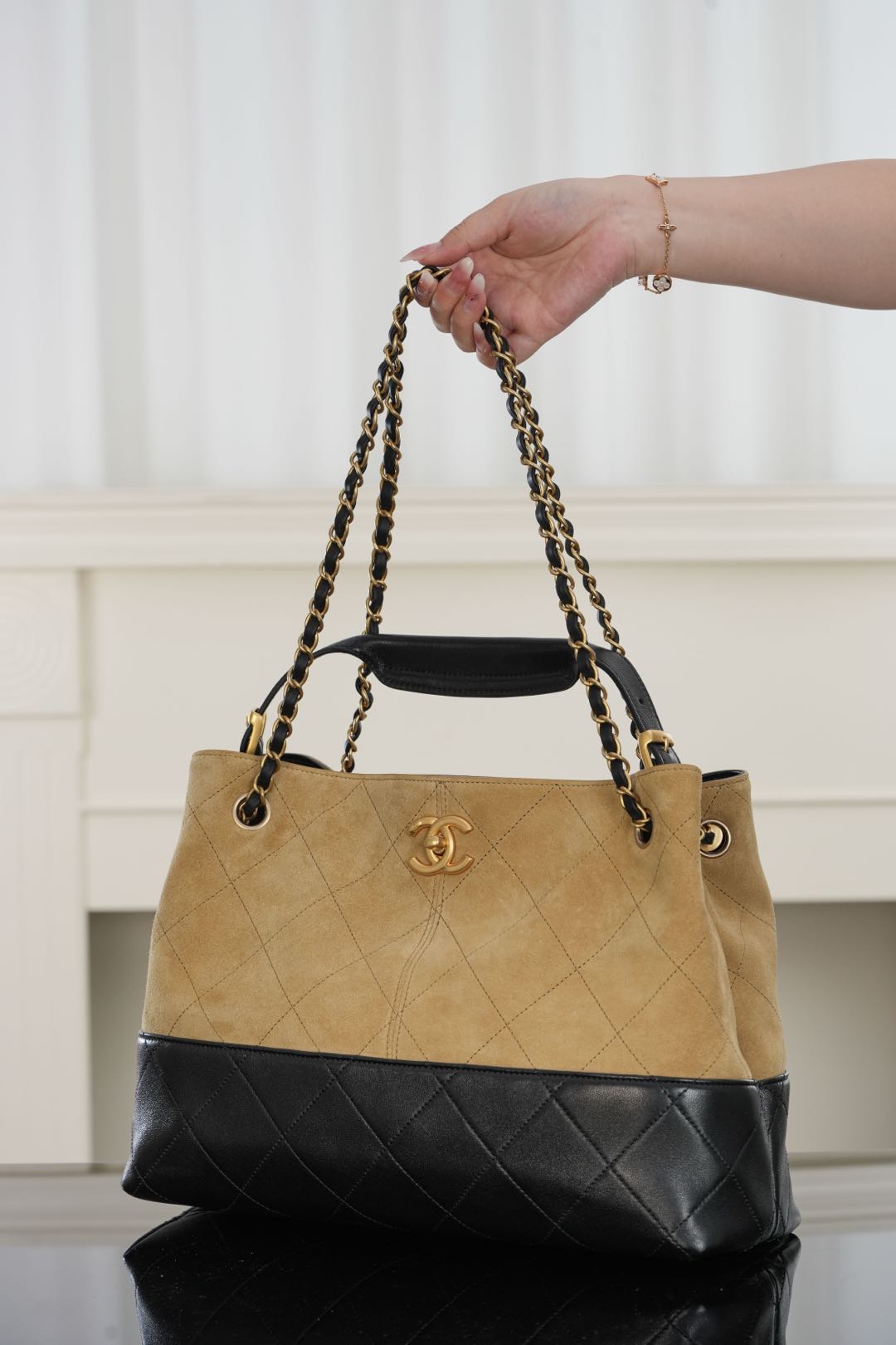 Tan and black quilted bag with chain handles and gold-tone logo, side view