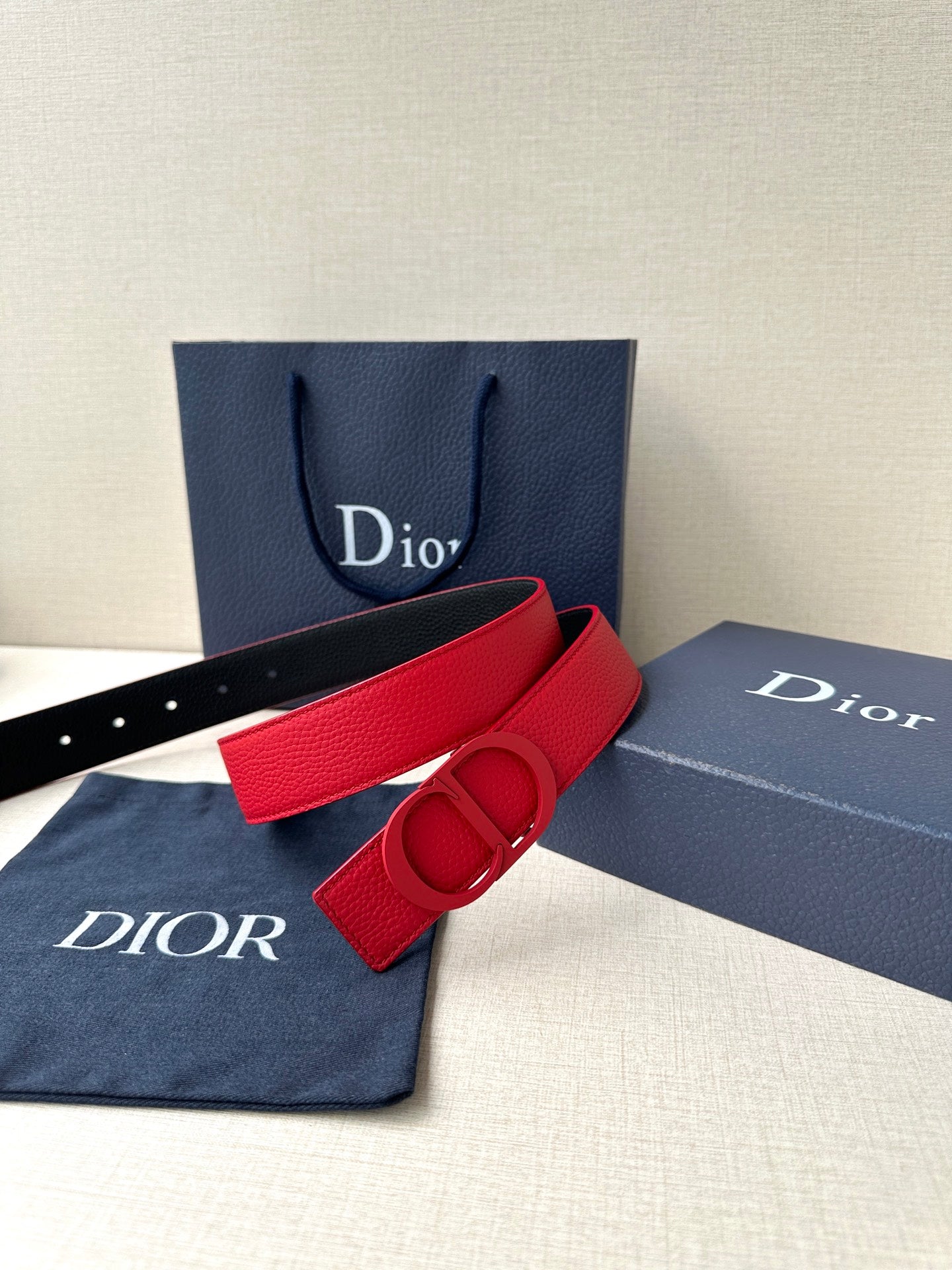 Red leather Dior belt with D buckle beside box and dust bag