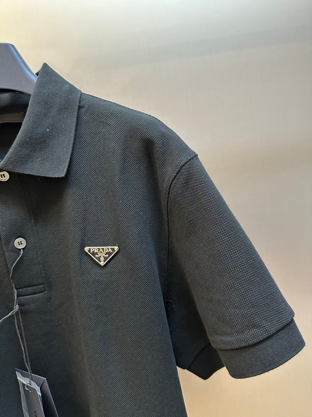 Prada polo shirt sleeve with triangular Prada logo patch on dark textured fabric