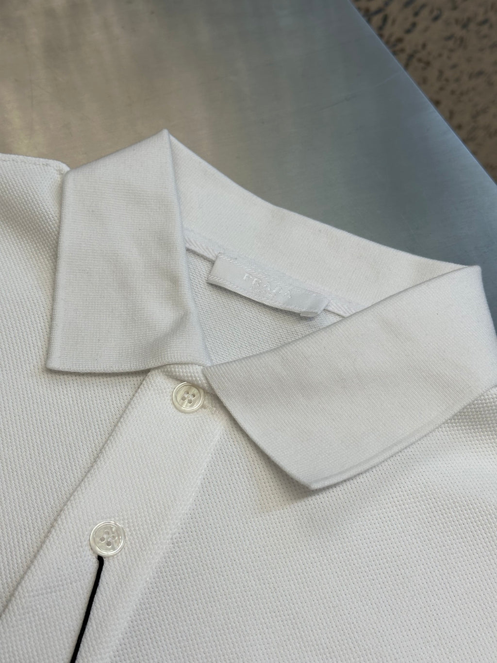 White Prada polo shirt collar and button placket with visible stitching and tags.