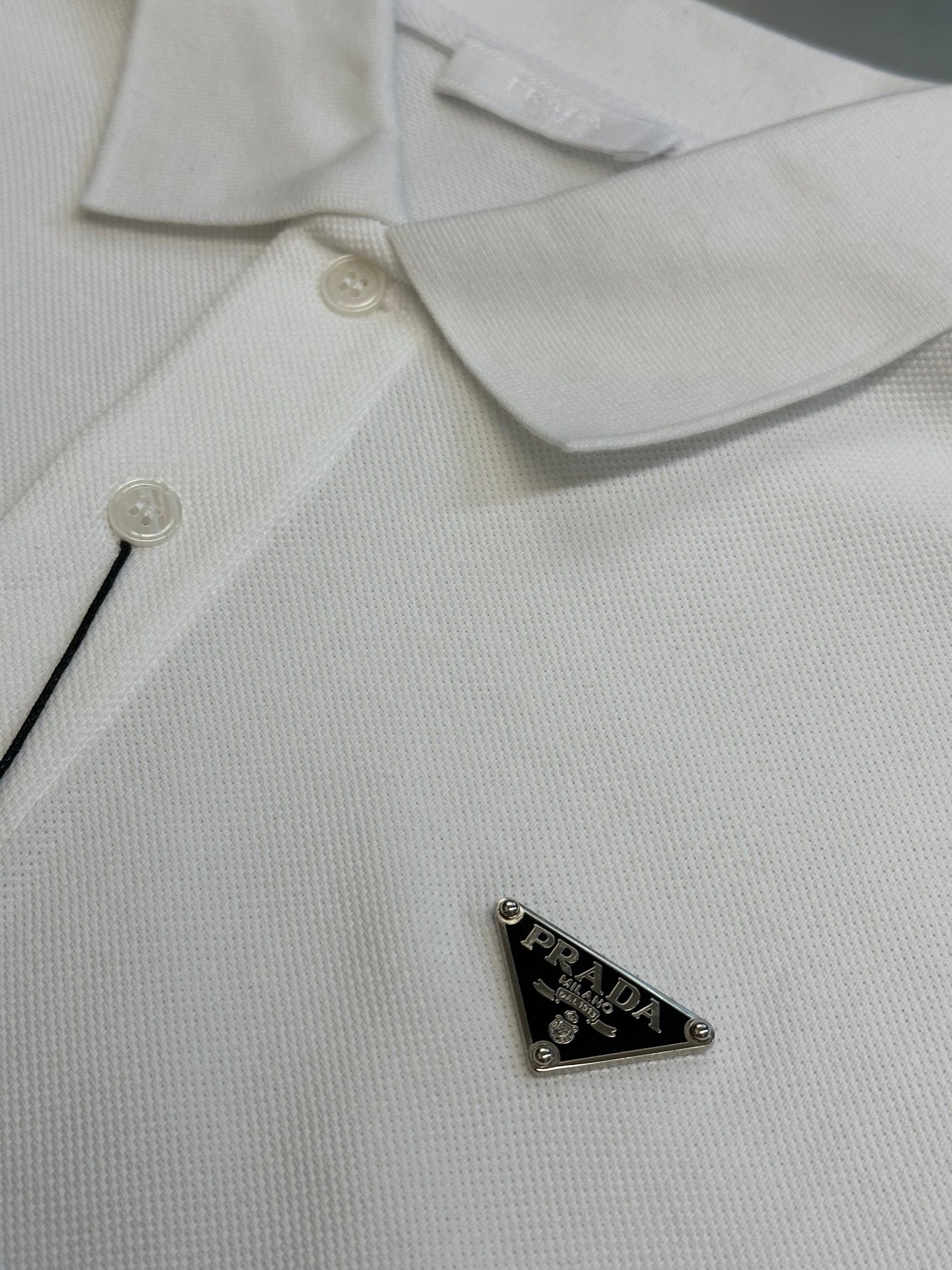 White polo shirt chest detail with button placket and triangular logo patch