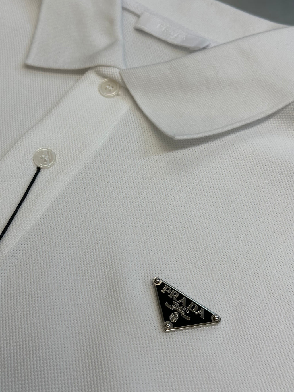 White Prada polo shirt chest close-up with small button and triangular logo patch.
