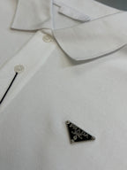 White Prada polo shirt chest close-up with small button and triangular logo patch.