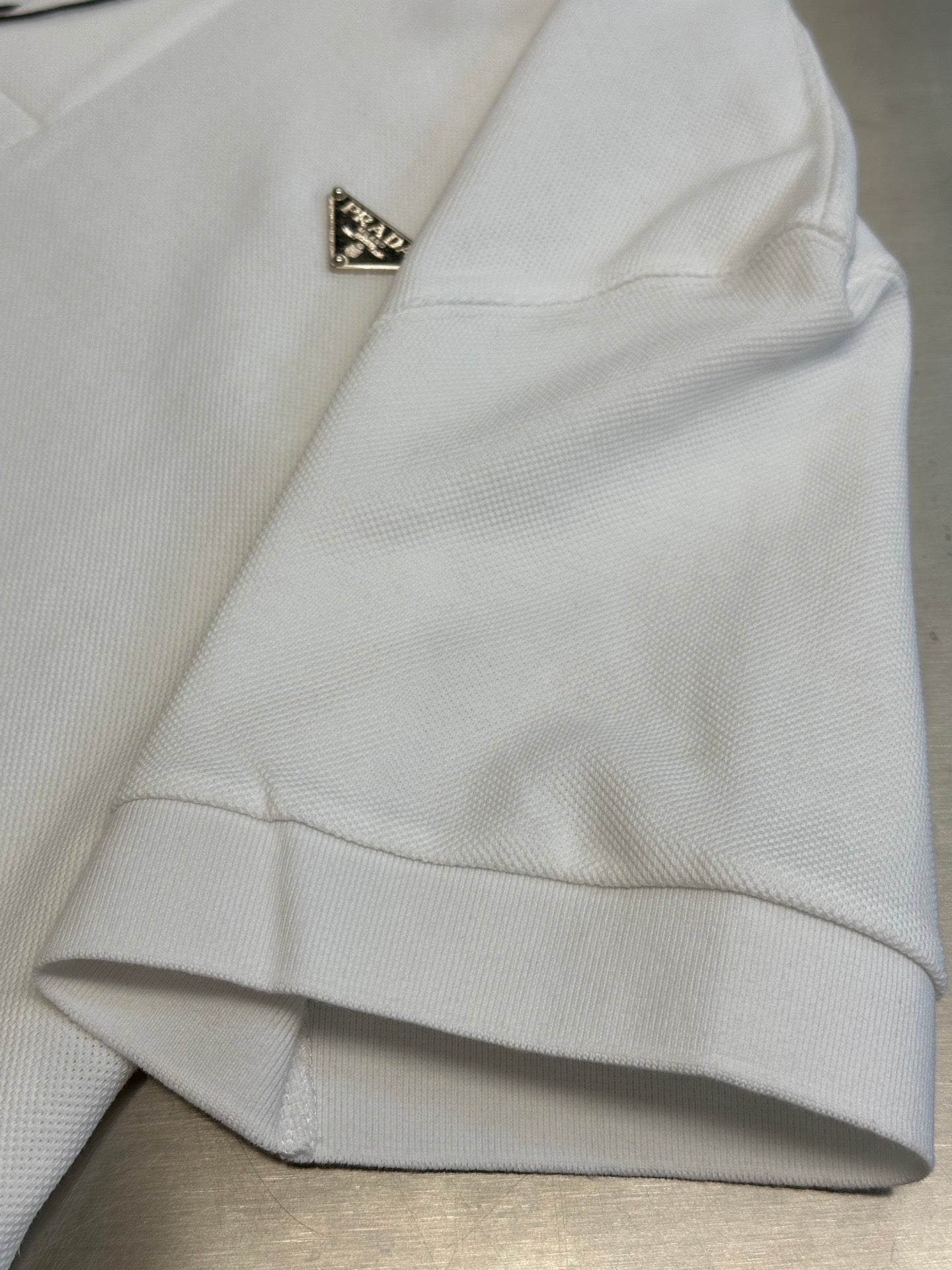 White Prada polo shirt sleeve hem and triangular logo detail.