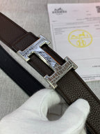 Leather belt buckle close-up on dark brown strap, silver frame with H motif