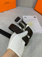 Leather belt with dark brown strap and silver H buckle, held in white glove