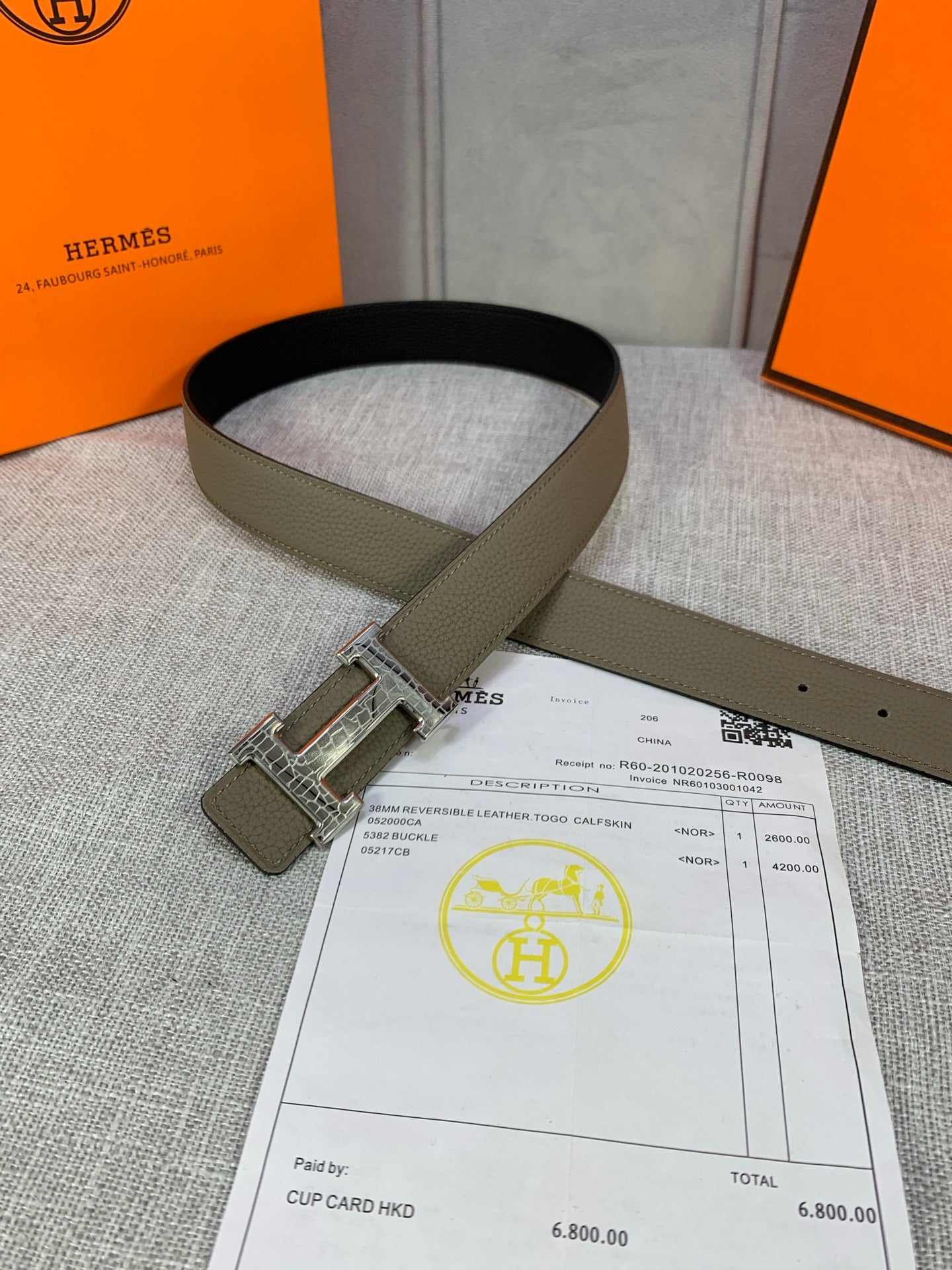 Olive leather belt looped on display with silver square buckle and strap holes.