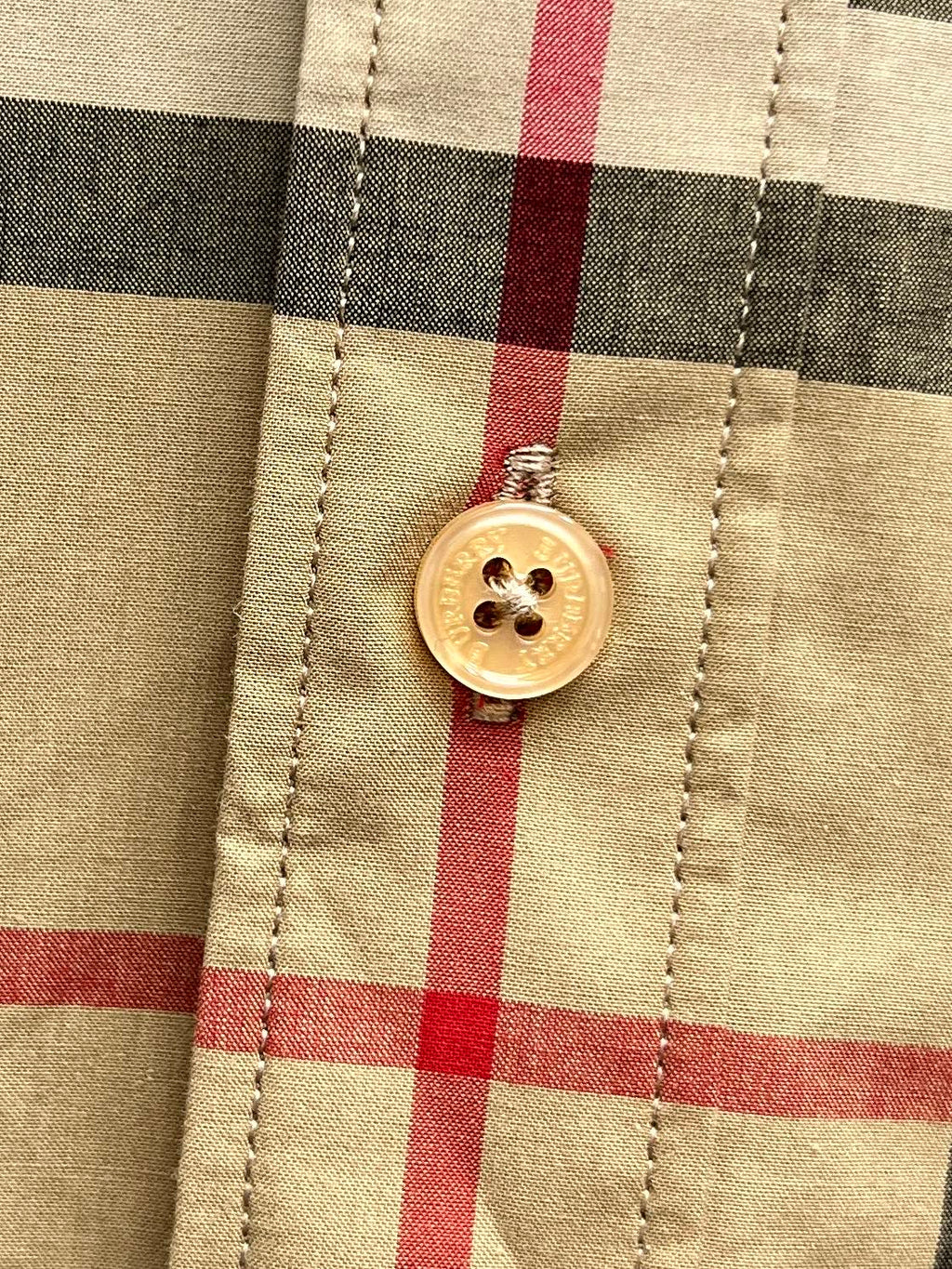 Burberry plaid shirt button detail close-up, round gold button on tan and black checks