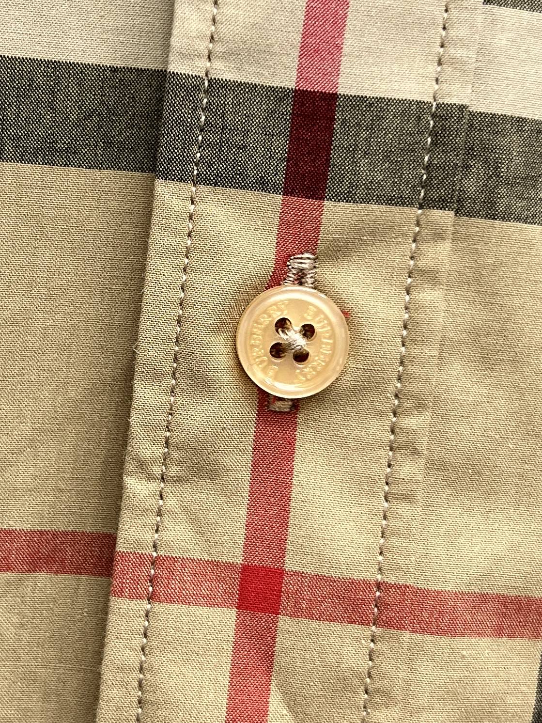 Burberry plaid shirt button detail close-up, round gold button on tan and black checks
