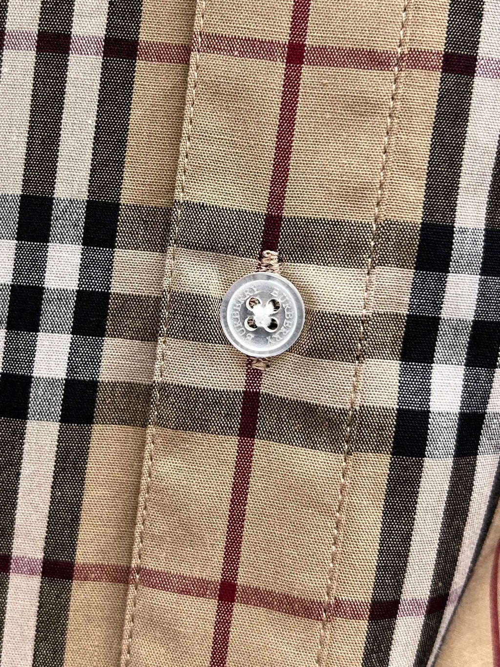 Placket button detail on a plaid shirt front with stitched seams