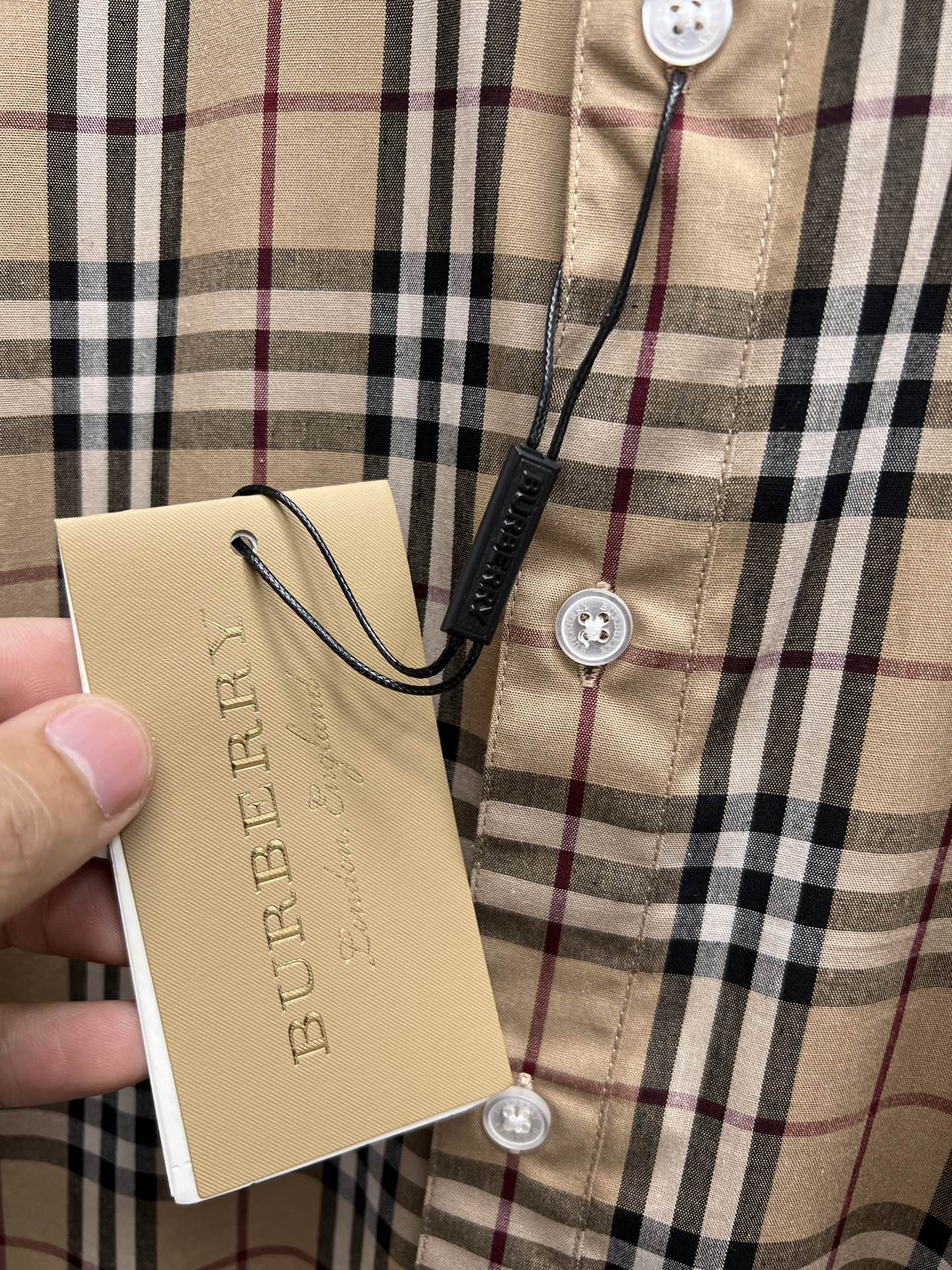 Plaid shirt front with button closure and attached tan brand hang tag