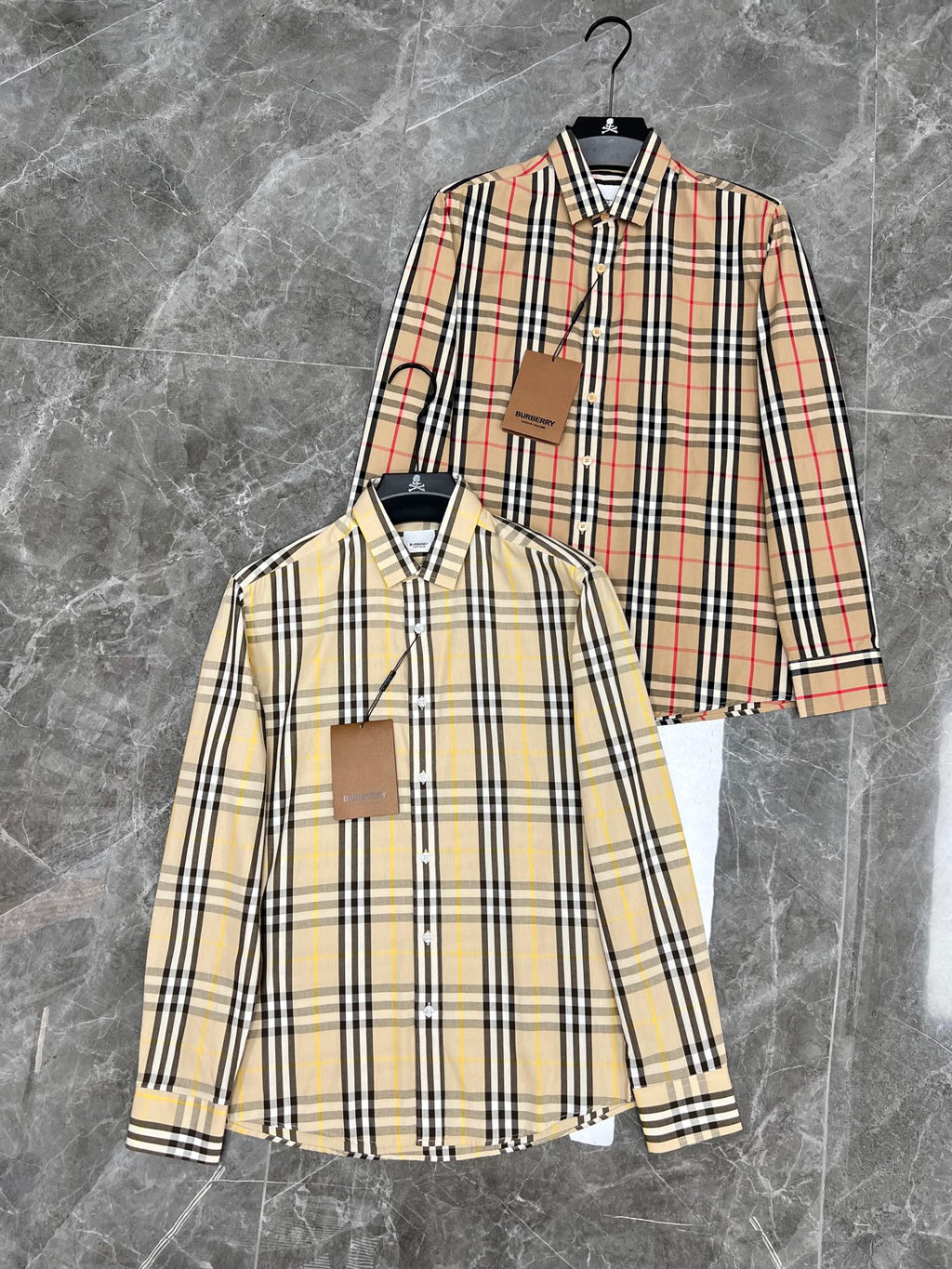 Two plaid button-up shirts on hangers, long sleeves and pointed collars, tan/black/red check