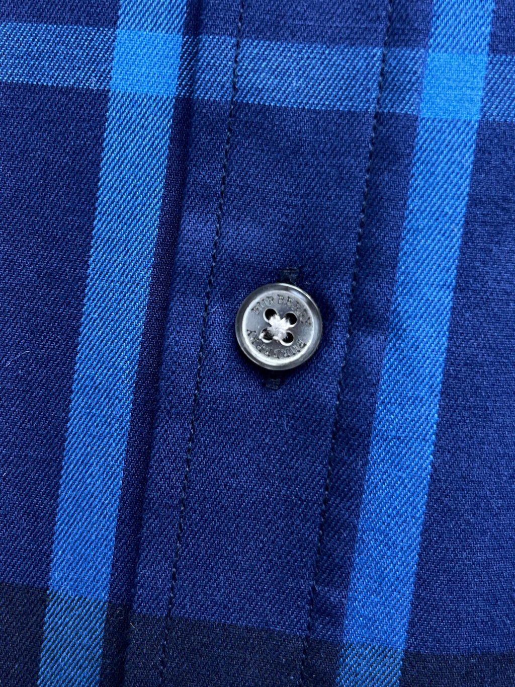 Round metal button on blue and white plaid shirt placket