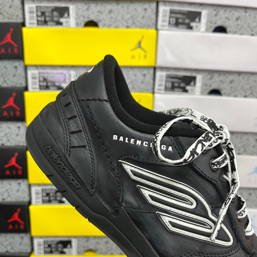 Black sneaker angled view with silver logo patch and patterned laces