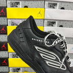 Black sneaker angled view with silver logo patch and patterned laces