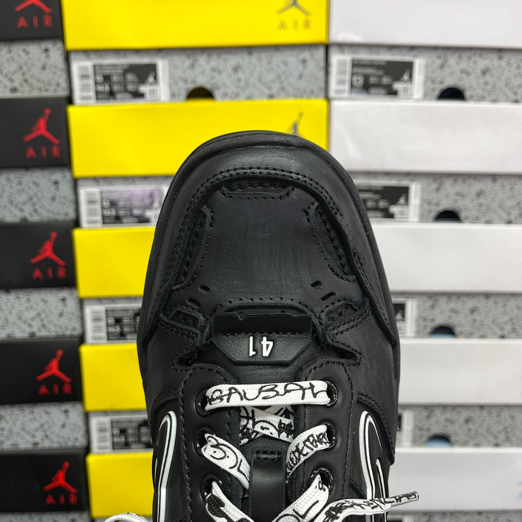 Black sneaker front view with logo tongue and patterned lace overlay