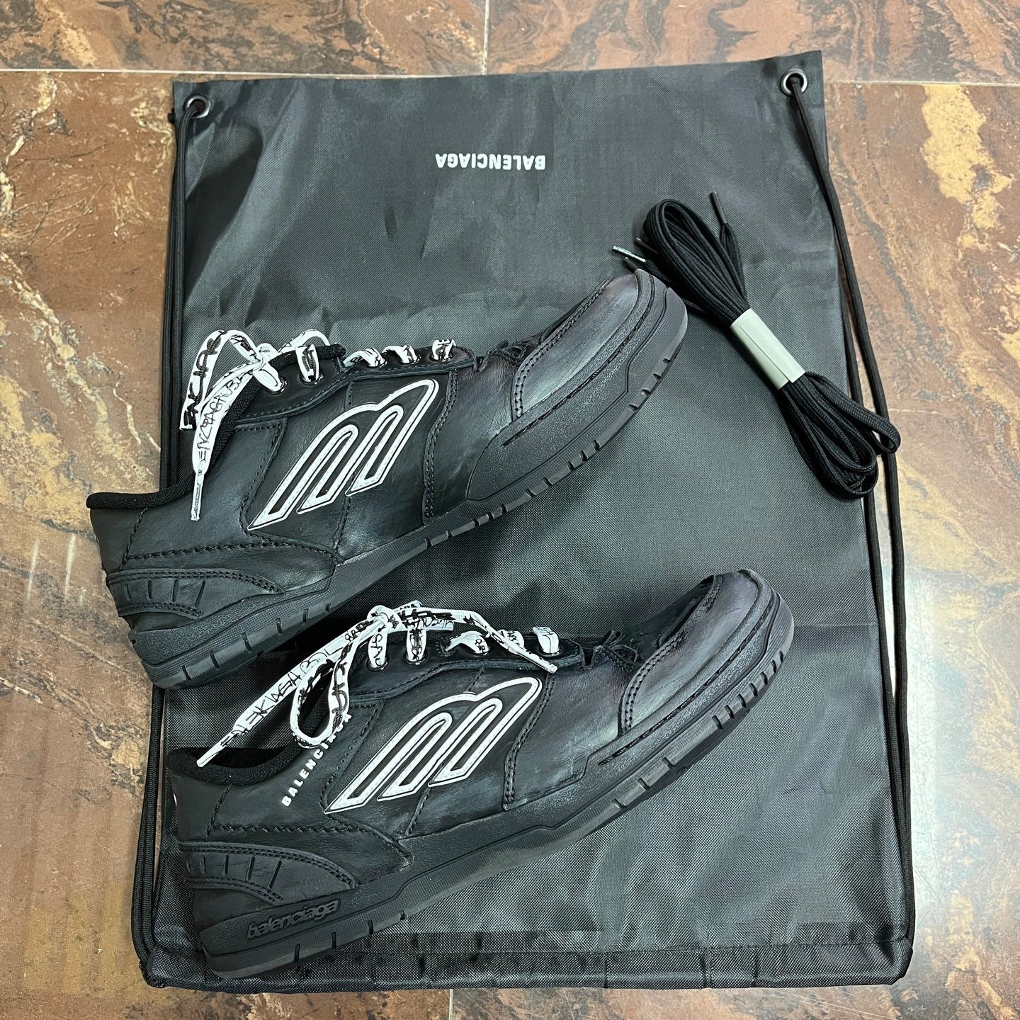 Black Balenciaga unisex sneakers with white logo, shown on drawstring pouch