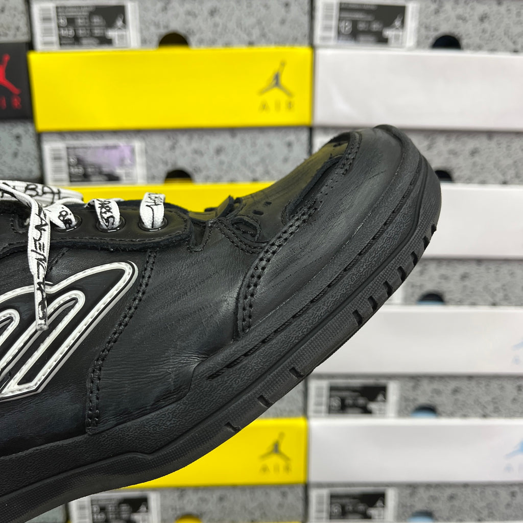 Black sneaker side view with silver logo and textured toe cap
