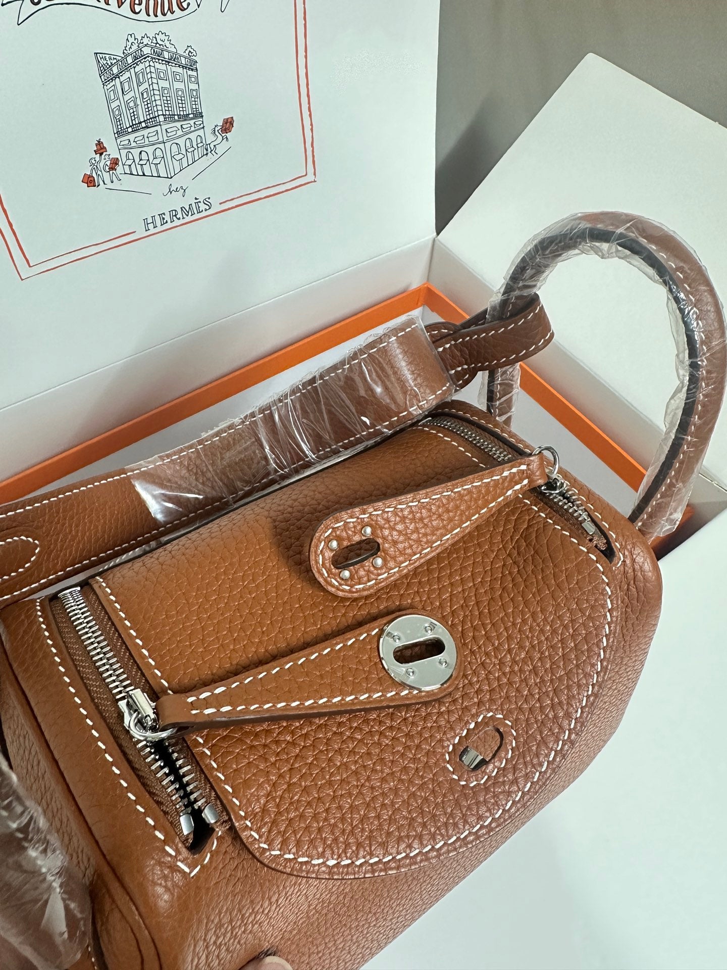 Hermes mini leather handbag front view in tan pebbled leather with zip pocket and flap