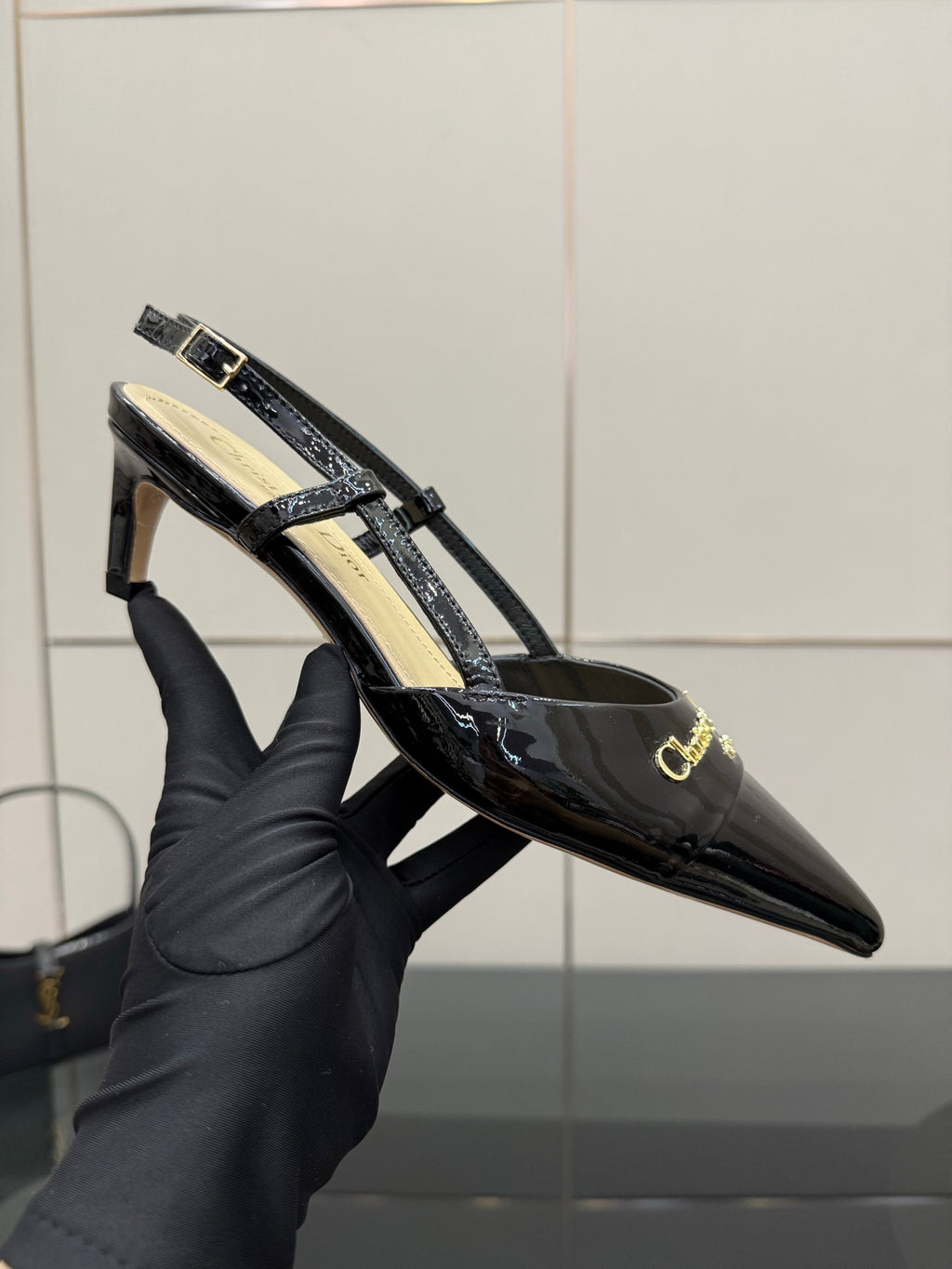Black patent slingback heel with gold logo buckle and strap detail