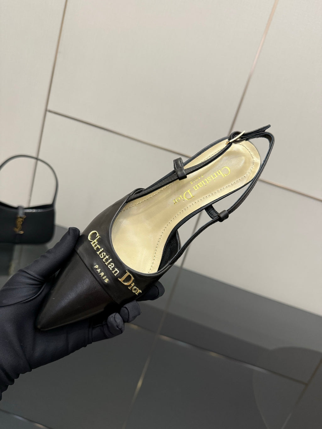 Close-up of black slingback pump held in hand, beige insole and thin straps