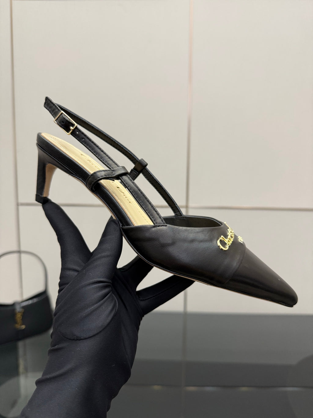 Close-up of black pointed slingback pump with high heel and gold emblem