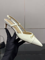 Ivory pointed-toe slingback mule heel held in gloved hand, gold trim detail