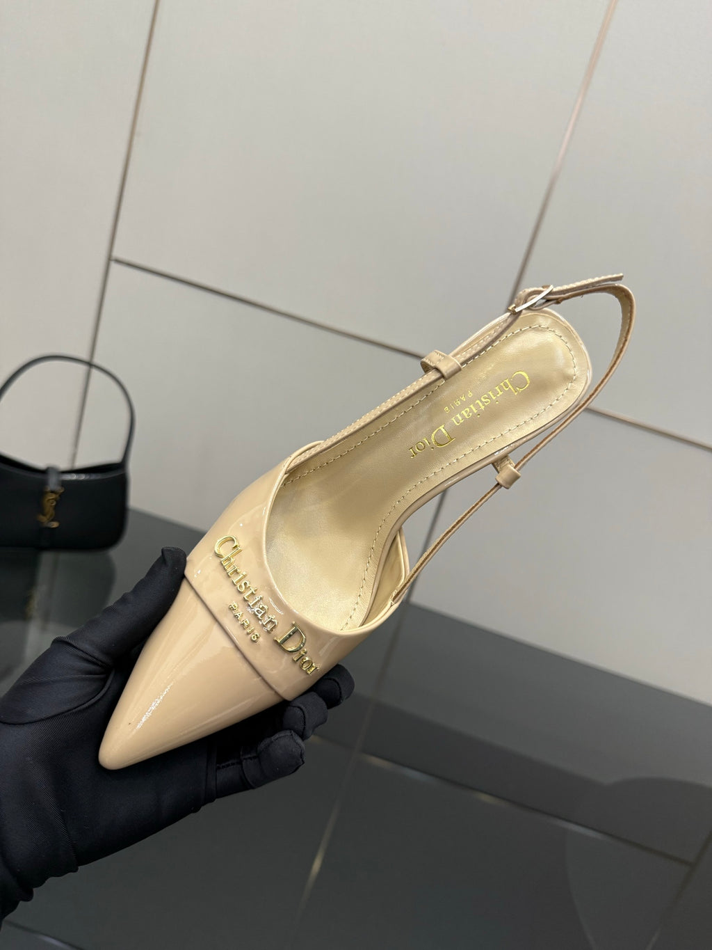 Beige point-toe slingback shoe held from side, showing logo on insole