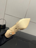 Beige point-toe slingback shoe held, showing side strap and decorative charm