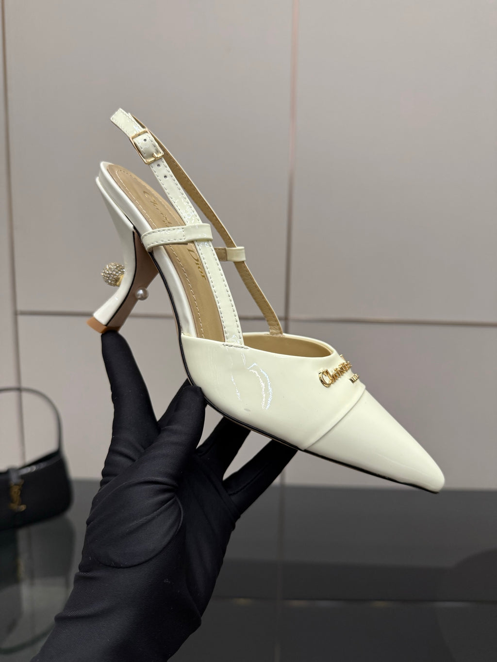 Ivory slingback pump held in hand, pointed toe, thin ankle strap, stiletto heel