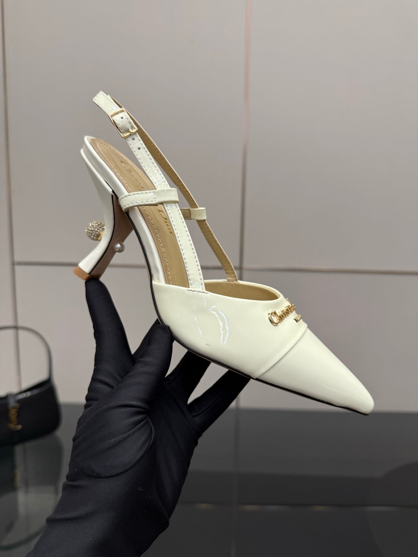 Ivory slingback pump held in hand, pointed toe, thin ankle strap, stiletto heel