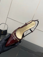 Dior ladies burgundy slingback heel held by black-gloved hand, side view.