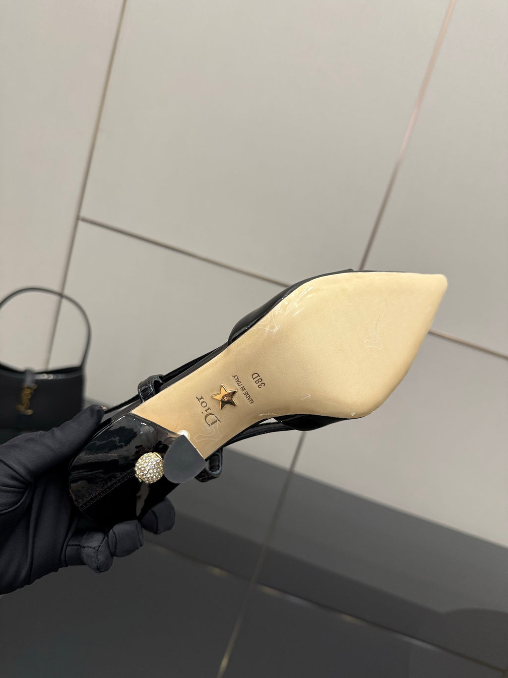 Black patent leather slingback heel underside in hand, cream insole with gold markings