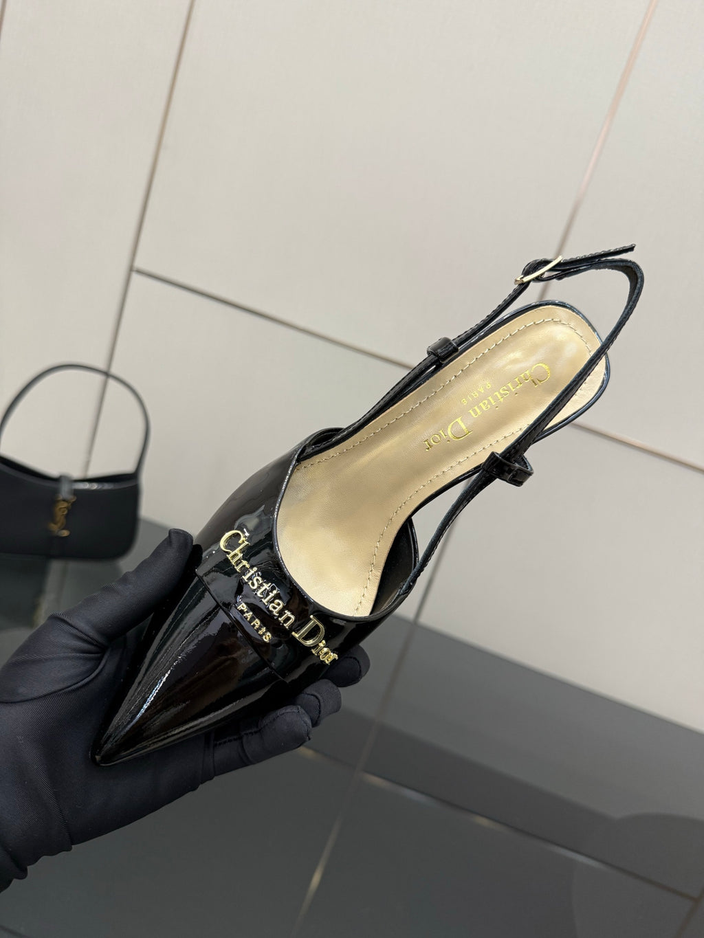 Black patent leather slingback heel in hand, interior lining and strap visible