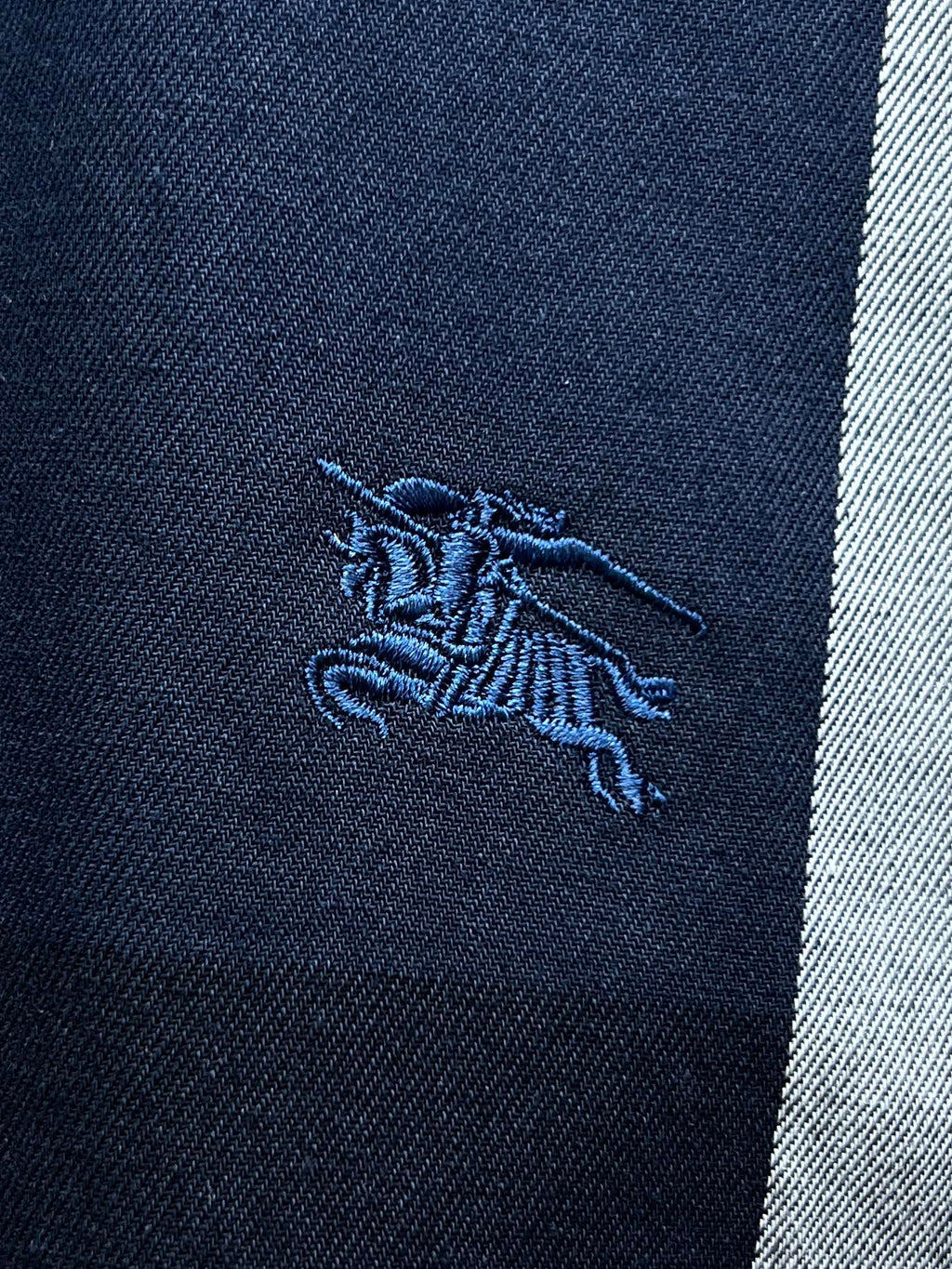 Embroidered horse logo on navy fabric of a plaid button-up shirt