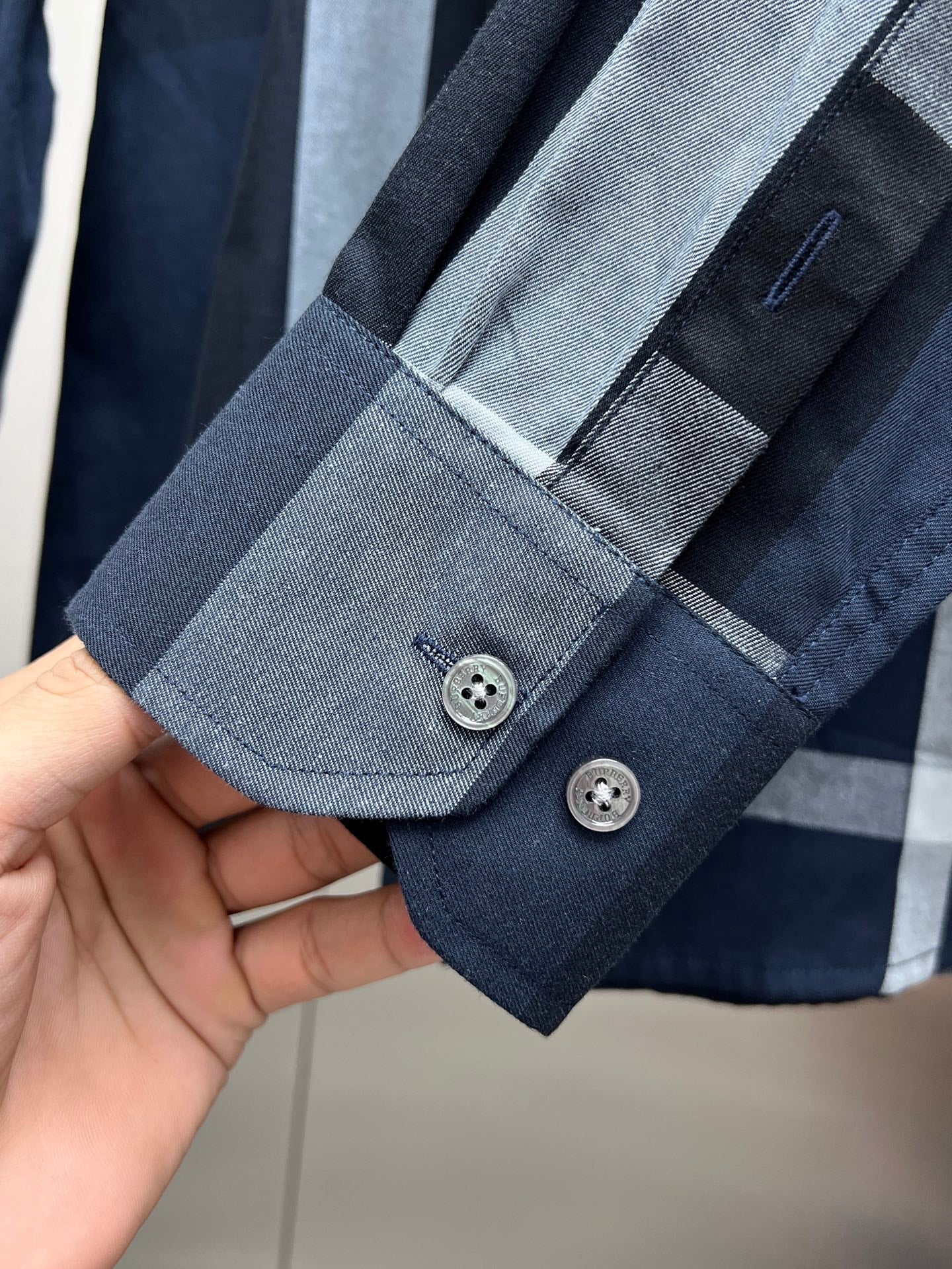 Navy long-sleeve shirt cuff with light blue plaid band and two-button closure