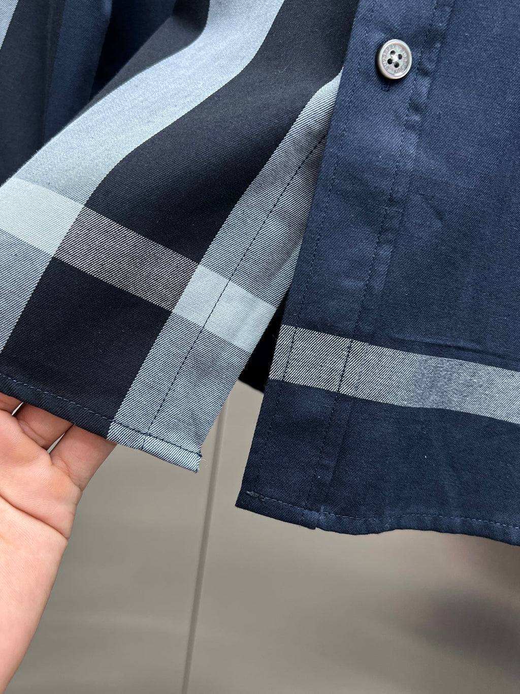 Navy long-sleeve shirt with light blue and gray plaid cuffs and buttoned placket
