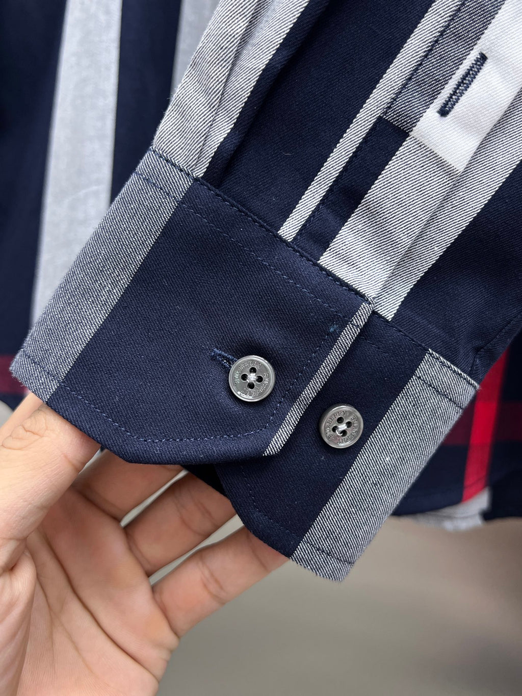 Long-sleeve check shirt cuff with button placket, navy and gray stripes with red accent