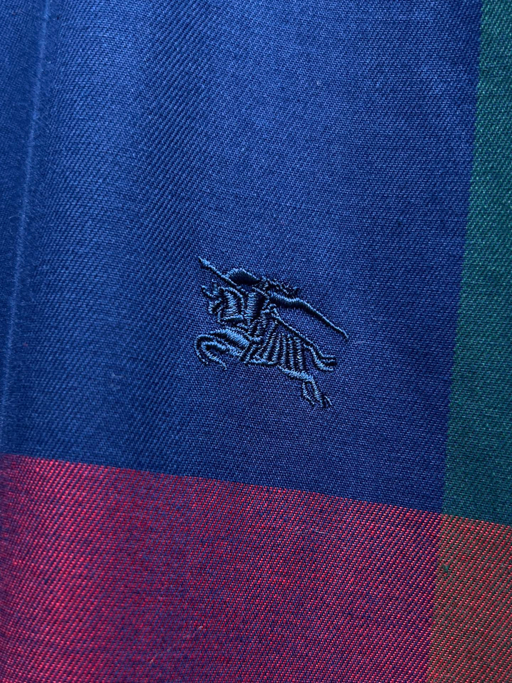 Embroidered Burberry horse logo on blue plaid fabric with purple and red bands