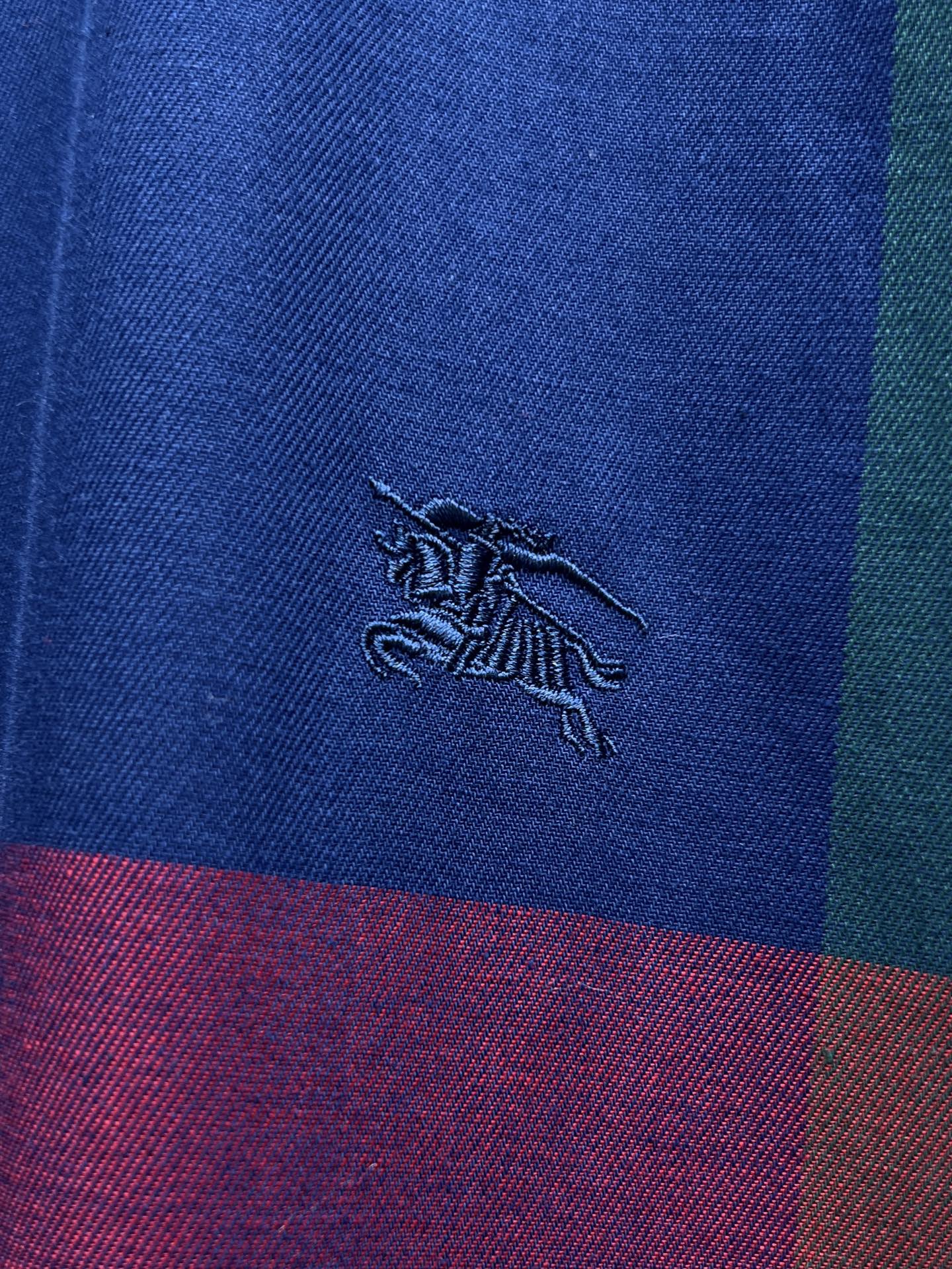 Embroidered Burberry horse logo on blue plaid fabric with purple and red bands