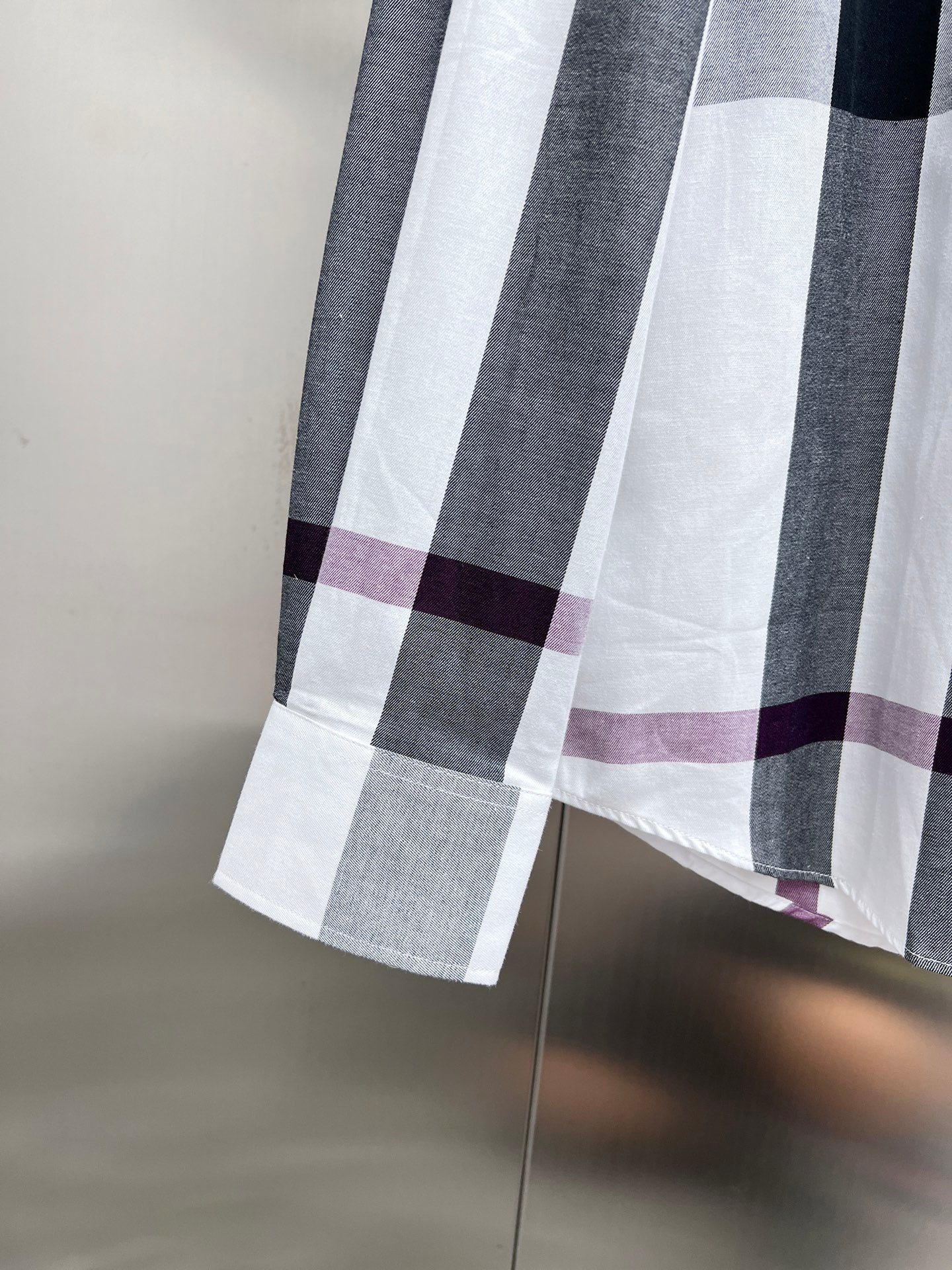 Long-sleeve button-up shirt hem in white, dark gray, and maroon plaid.
