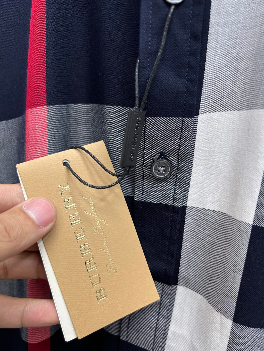 Front of plaid button-up shirt with gold hang tag and navy, gray, and red