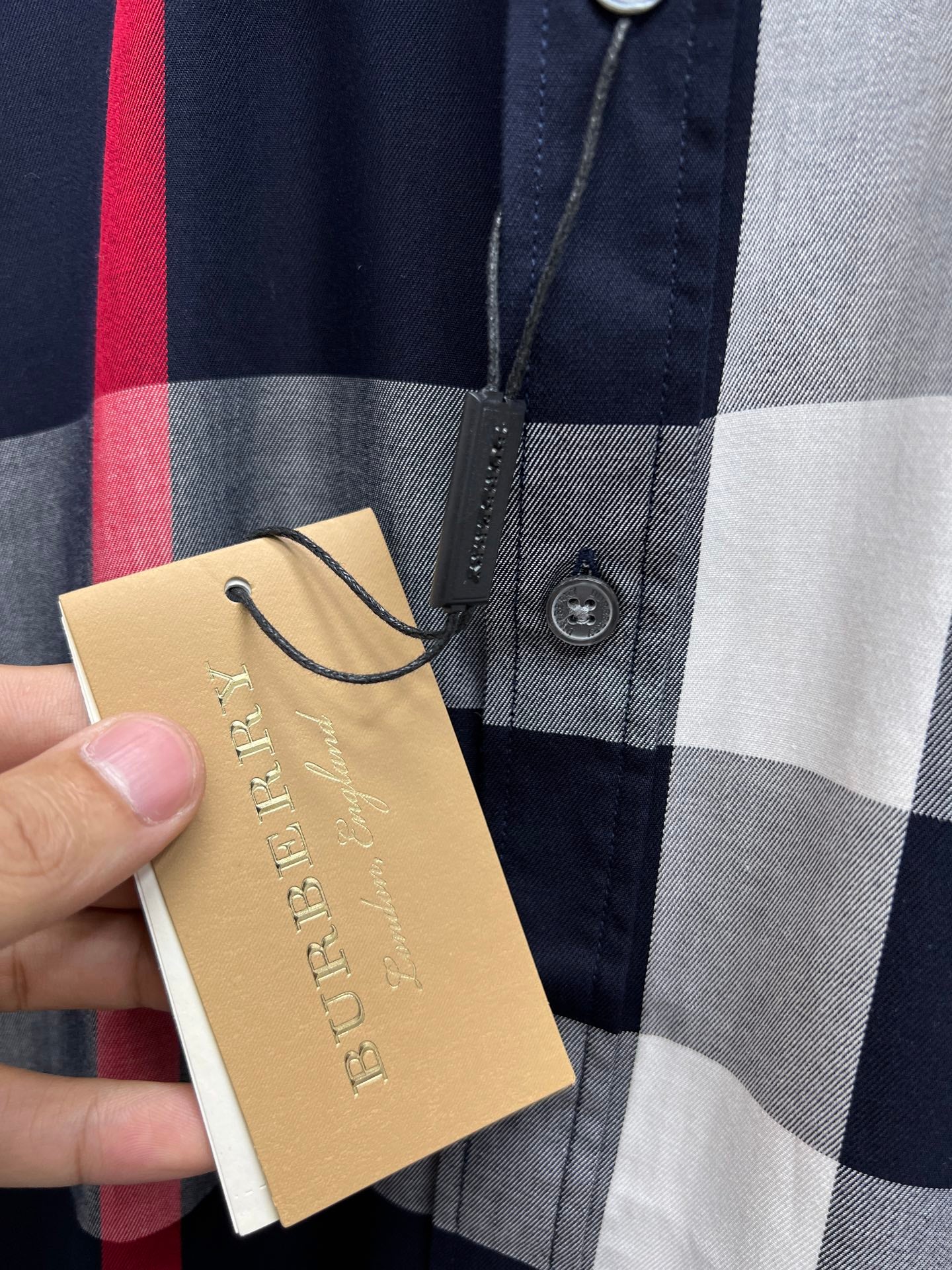 Front of plaid button-up shirt with gold hang tag and navy, gray, and red