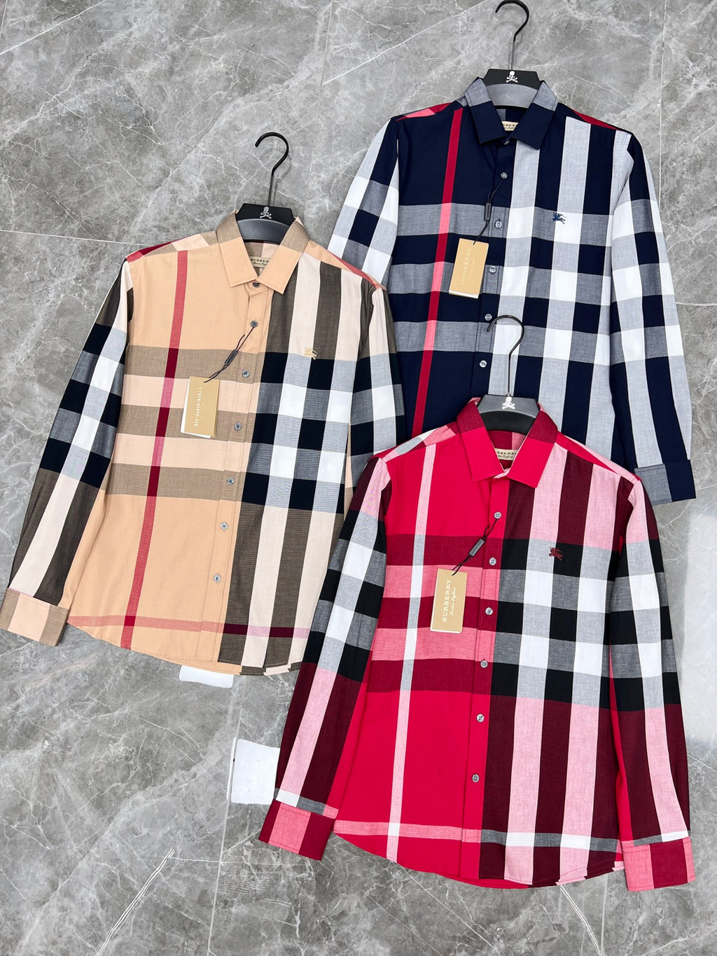 Three plaid long-sleeve button-up shirts on hangers: beige, navy, and red